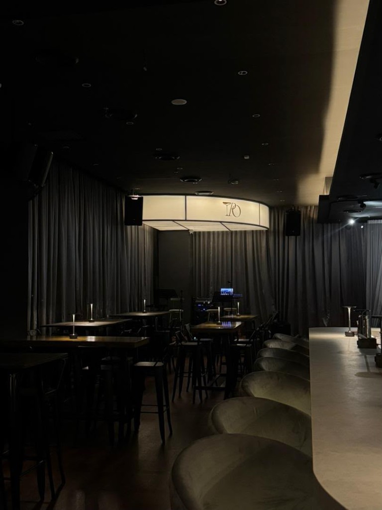 Dim lounge seating and glowing stage light at Tipsy Plus One